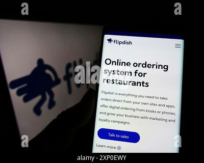 Stuttgart, Allemagne, 03-29-2022, une personne tenant un téléphone portable avec le site de la société irlandaise Flipdish Limited sur l'écran devant le logo. Concentrez-vous sur Banque D'Images