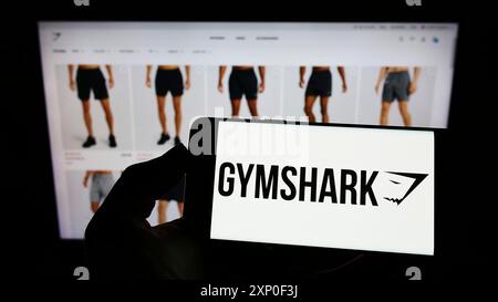 Stuttgart, Allemagne, 03-30-2022, personne tenant un téléphone portable avec le logo de la société de vêtements britannique Gymshark Limited sur l'écran devant l'entreprise Banque D'Images