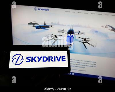 Personne tenant le téléphone portable avec le logo de la compagnie d'aviation japonaise SkyDrive Inc. sur l'écran en face de la page Web d'affaires. Concentrez-vous sur l'affichage du téléphone Banque D'Images