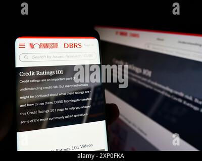 Stuttgart, Allemagne, 03-06-2022 : personne tenant un smartphone avec le site Web de la société canadienne de notation de crédit DBRS Morningstar sur l'écran avec moniteur. Banque D'Images