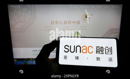 Personne tenant un smartphone avec le logo de la société chinoise Sunac China Holdings Limited sur l'écran en face du site Web. Concentrez-vous sur l'affichage du téléphone Banque D'Images