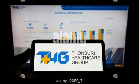 Stuttgart, Allemagne, 01-29-2022, personne tenant un smartphone avec le logo de la société thaïlandaise Thonburi Healthcare Group (THG) sur l'écran devant le site Web. Banque D'Images