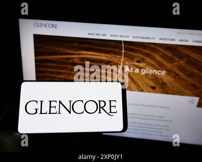 Stuttgart, Allemagne, 01-28-2022, personne tenant le téléphone portable avec le logo de la société de négoce de marchandises Glencore plc sur l'écran en face de la page Web d'affaires. Banque D'Images
