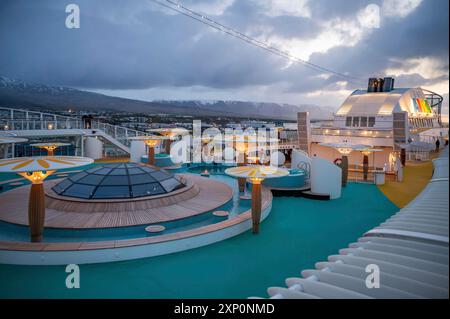 Pont de bateau illuminé du bateau de croisière AIDA Bella dans la soirée, fjord avec chaîne de montagnes de l'Islande en arrière-plan, grand angle de vue Banque D'Images