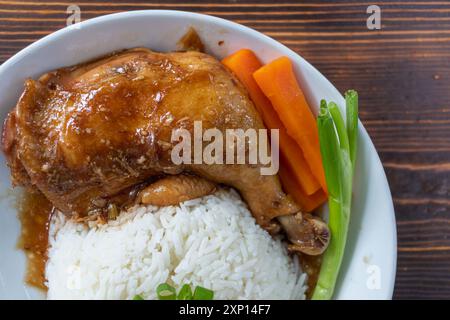 Cuisses et pilons de poulet rôtis sont servis avec du riz au jasmin et des légumes frais dans une assiette blanche. Cuisses de poulet cuites dans sucré et délicieux Banque D'Images