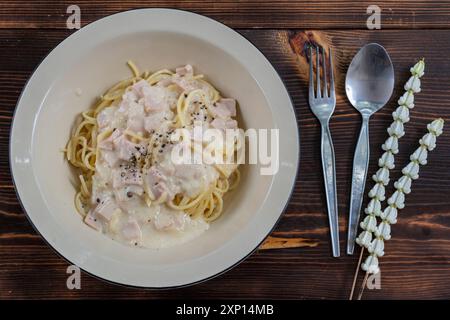 spaghetti carbonara, un délicieux mélange de jambon, bacon et fromage chaud, servi dans une assiette blanche sur une table en bois prête à manger. Délicieux spaghettis avec env Banque D'Images