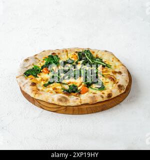 Pizza à la croûte fine, garnie d'épinards, de tomates et de fromage, servie sur une planche de bois Banque D'Images