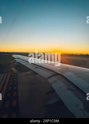 L'aile d'un avion est vue au premier plan de l'image, avec le coucher du soleil en arrière-plan. Le ciel est un beau mélange d'orange et de rose Banque D'Images