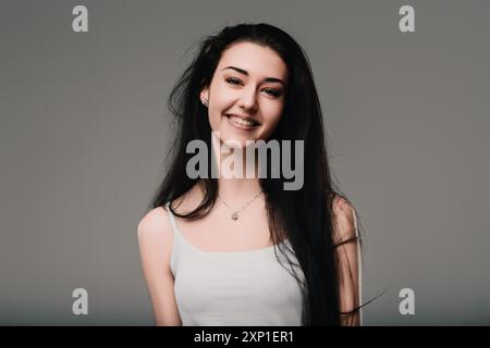 La jeune femme aux longs cheveux foncés sourit tout en étant perdue dans ses pensées. Son expression agréable suggère une humeur positive et contemplative Banque D'Images