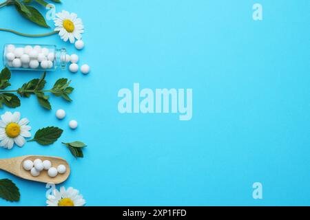 Homéopathie. Bouteille en verre, pilules, camomilles et feuilles vertes sur fond bleu clair, pose plate. Espace pour le texte Banque D'Images