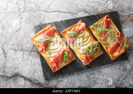 Apéritif feuilleté cuit au four festif avec poire, jamon et roquette gros plan sur un panneau de marbre sur la table. Vue horizontale de dessus Banque D'Images