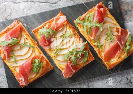 Tartes à pâte feuilletée salées avec poire, jamon et roquette gros plan sur une planche de marbre sur la table. Vue horizontale de dessus Banque D'Images