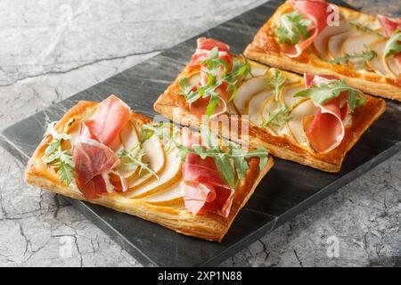 Grignoter des sandwichs feuilletés ouverts avec poire, jamon et roquette en gros plan sur une planche de marbre sur la table. Horizontal Banque D'Images