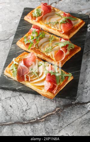 Délicieuses pâtisseries feuilletées cuites au four avec poire, fromage à la crème, jamon et roquette gros plan sur panneau de marbre sur la table. Vertical Banque D'Images