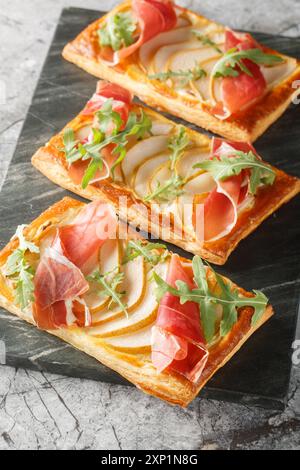 Tartes feuilletées à la poire jambon pour buffet et soirées gros plan sur planche de marbre sur table. Vertical Banque D'Images