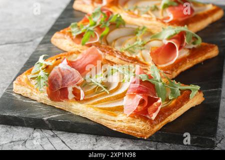 Apéritif feuilleté cuit au four festif avec poire, jamon et roquette gros plan sur un panneau de marbre sur la table. Horizontal Banque D'Images