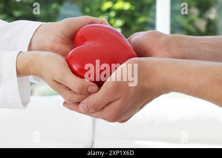 Docteur donnant le coeur rouge au patient à la table blanche en clinique, gros plan Banque D'Images