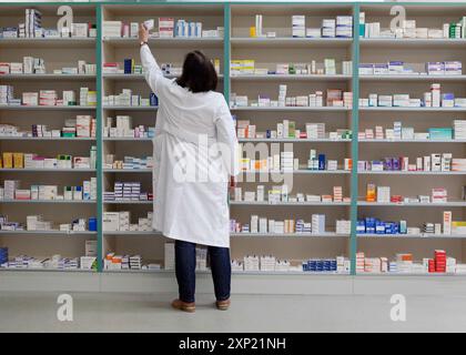 Pharmacien cherchant des médicaments sur les étagères d'une pharmacie allemande. La médecine organisée en milieu pharmaceutique. Banque D'Images