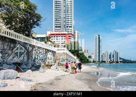 Une famille marchant le long de la plage de Tanjing Tokong à Penang, Malaisie avec de grands gratte-ciel modernes, une partie d'un paysage urbain en arrière-plan. Banque D'Images