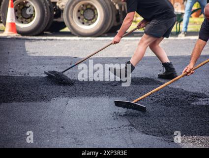 Les ouvriers qui resurfaçent une allée avec de l'asphalte à l'aide de râteaux, montrant un gros plan d'un processus de construction d'entraînement d'asphalte. Banque D'Images