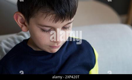 Gros plan d'un jeune garçon regardant en bas avec une expression sereine et concentrée. Banque D'Images