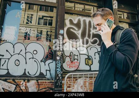 Manhattan, New York, États-Unis, 18 avril 2022. Un homme en noir parle au téléphone devant un bâtiment en brique avec du graphite en arrière-plan Banque D'Images