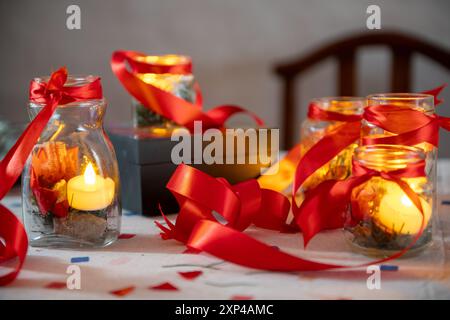 Des bougies chaudes dans des pots avec des rubans rouges créent une atmosphère festive chaleureuse. Banque D'Images