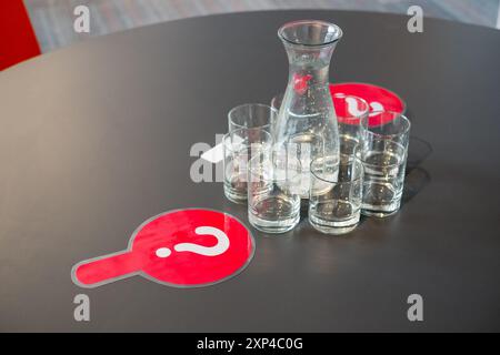 Carafe à eau et verres sur table noire avec deux signes de point d'interrogation rouge Banque D'Images