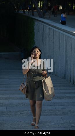 Une femme parle sur son téléphone portable tout en descendant un escalier. Elle porte un sac marron et un sac à main Banque D'Images