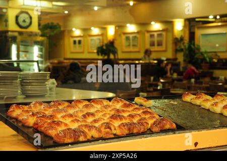 Croissants fraîchement cuits sur un plateau dans un café de boulangerie confortable avec un éclairage chaleureux Banque D'Images