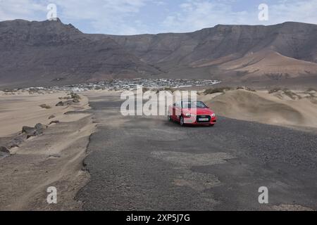 La route allant des bungalows Los Noruegos à la Caleta de Famara, avec une Audi cabriolet rouge solitaire. Famara, Lanzarote. Banque D'Images