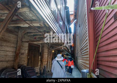 Bergen, Norvège - 30 avril 2024 : les touristes visitent une ruelle étroite bordée de maisons en bois colorées dans le quartier historique de Bryggen à Bergen. Banque D'Images