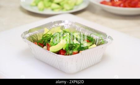 Mains de chef, sauce vinaigrée versant dans une salade de légumes avec avocat et algues hiyashi de gros plan. Livraison d'aliments sains et diététiques. Préparer des repas sains dans une boîte de récipient sur la cuisine professionnelle Banque D'Images