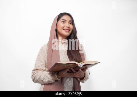 Femme musulmane asiatique sérieuse portant le voile hijab priant et lisant Al Coran, debout sur fond blanc isolé. Ramadan et Aïd Moubarak concept Banque D'Images