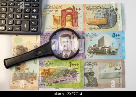 Billets de banque avec loupe et calculatrice. Le portrait du président Bachar al-Assad est focalisé dans la loupe Banque D'Images