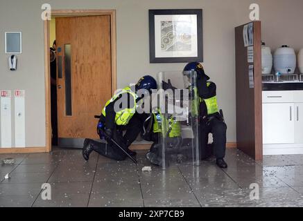 Les policiers s'occupent d'un collègue blessé à l'intérieur de l'hôtel vu par une fenêtre brisée alors que des troubles s'allument lors d'une manifestation anti-immigration devant le Holiday Inn Express à Rotherham, dans le South Yorkshire. Date de la photo : dimanche 4 août 2024. Banque D'Images