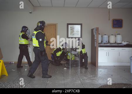 Les policiers s'occupent d'un collègue blessé à l'intérieur de l'hôtel vu par une fenêtre brisée alors que des troubles s'allument lors d'une manifestation anti-immigration devant le Holiday Inn Express à Rotherham, dans le South Yorkshire. Date de la photo : dimanche 4 août 2024. Banque D'Images