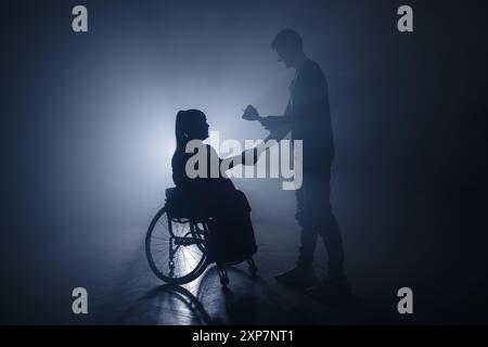 Silhouette masculine félicitant et donnant un trophée de victoire à une femme en fauteuil roulant célébrant la réussite en élevant la coupe gagnante. Banque D'Images