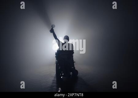 Femme handicapée physique recevant une coupe de victoire d'un homme assis dans un fauteuil roulant dans une pièce sombre avec un rétroéclairage blanc. Banque D'Images