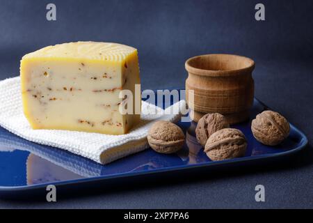 Un plateau magnifiquement agencé comprend un coin de fromage artisanal infusé d'herbes, entouré de noix entières et d'un petit bol en bois. Banque D'Images