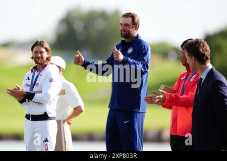 Scottie Scheffler, l'américain, cède la tête après avoir remporté une médaille d'or à la suite de la quatrième manche individuelle masculine, alors que le Britannique Tommy Fleetwood applaudit au Golf National, le neuvième jour des Jeux Olympiques de Paris 2024 en France. Date de la photo : dimanche 4 août 2024. Banque D'Images