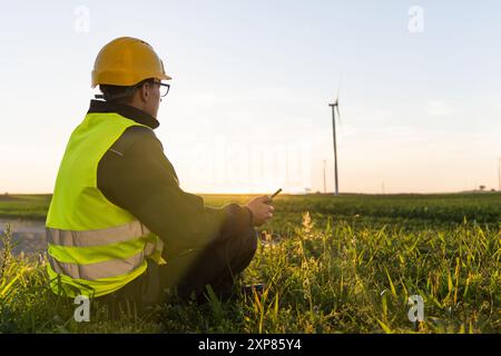 Le travailleur est assis sur l'herbe et regarde les éoliennes. Banque D'Images