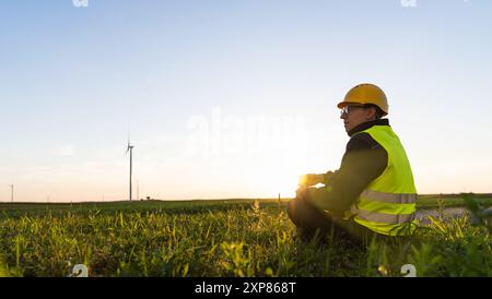 Le travailleur est assis sur l'herbe et regarde les éoliennes. Banque D'Images