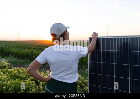 Femme portant un chapeau blanc se tient à côté du panneau solaire au coucher du soleil. Banque D'Images