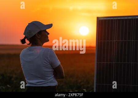 Femme portant un chapeau blanc se tient à côté du panneau solaire au coucher du soleil. Banque D'Images