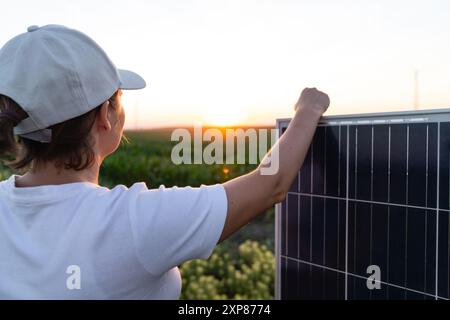 Femme portant un chapeau blanc se tient à côté du panneau solaire au coucher du soleil. Banque D'Images