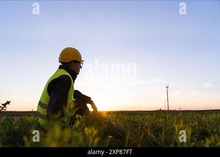 Le travailleur est assis sur l'herbe et regarde les éoliennes. Banque D'Images