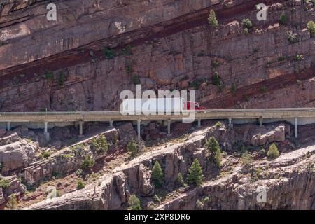 Semi-camion conduisant le long de la route de montagne avec des falaises rocheuses en arrière-plan Banque D'Images