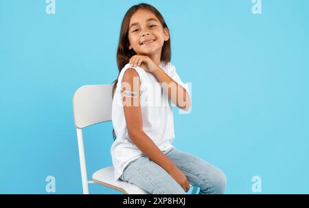 Fille heureuse vaccinée montrant le bras après la vaccination, fond bleu Banque D'Images