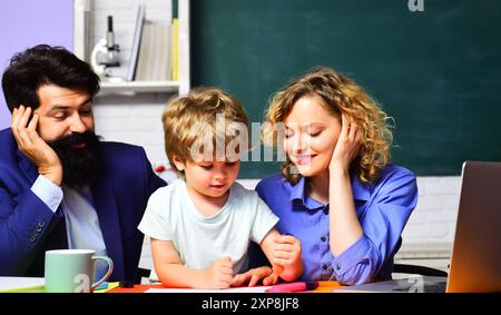 Les enseignants homme et femme aidant l'enfant de l'école primaire font les travaux scolaires. Leçon privée. Garçon mignon de l'école primaire faisant ses devoirs avec le père A. Banque D'Images